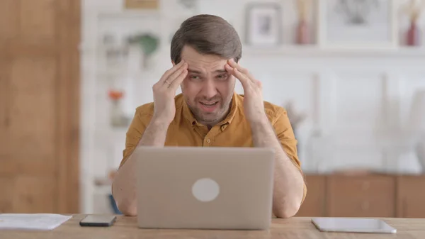 Mladý muž s bolestí hlavy při práci na notebooku — Stock fotografie