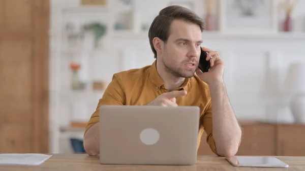 Wütender junger Mann telefoniert mit Laptop im Büro — Stockfoto