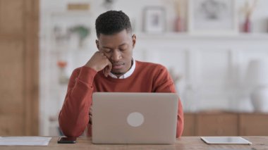 Yorgun Afrikalı adam dizüstü bilgisayarla ofiste otururken uyukluyor