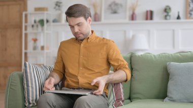 Genç adam kanepeye oturdu, dizüstü bilgisayar açılıyor.