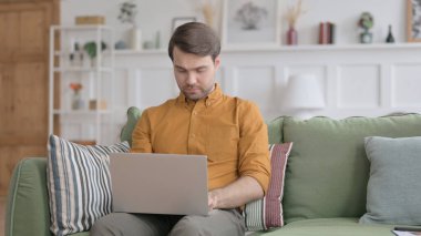 Genç adam kanepede dizüstü bilgisayarda çalışıyor.