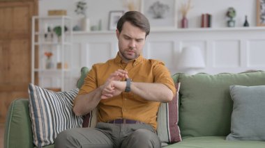 Genç adam koltukta otururken Smart Watch kullanıyor.