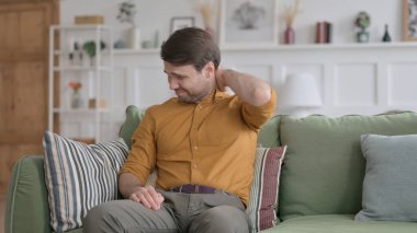 Genç adam koltukta otururken boynu ağrıyor.