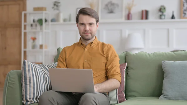 Jeune homme regardant la caméra tout en utilisant un ordinateur portable dans le bureau — Photo