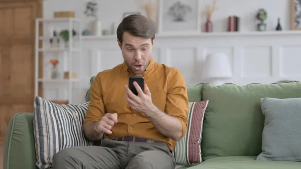 Junger Mann reagiert auf Erfolg mit Smartphone zu Hause — Stockfoto