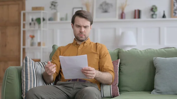 Jeune homme réagissant à la perte sur documents, Sofa — Photo