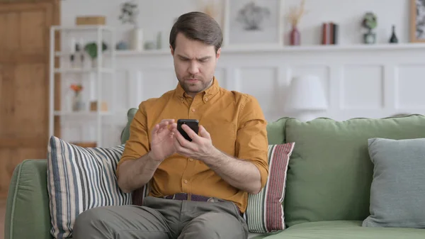 Nuori mies käyttää älypuhelinta sohvalla — kuvapankkivalokuva