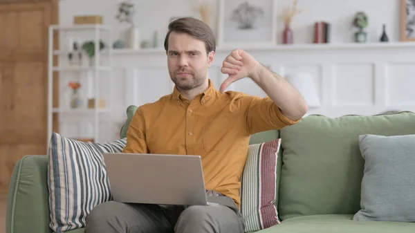 Junger Mann zeigt Daumen-runter-Zeichen, während er Laptop im Büro benutzt — Stockfoto