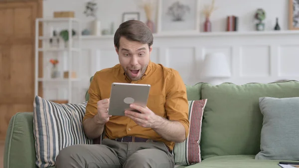 Jeune homme célébrant le succès sur tablette sur canapé — Photo