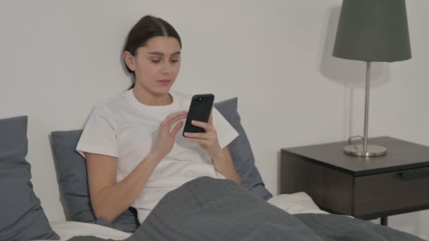 ベッドの中でスマートフォンに損失に反応ヒスパニック女性 — ストック動画
