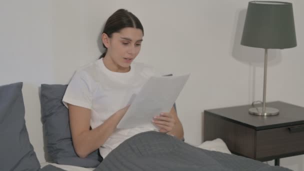 Hispanic kvinna firar när du läser dokument i sängen — Stockvideo