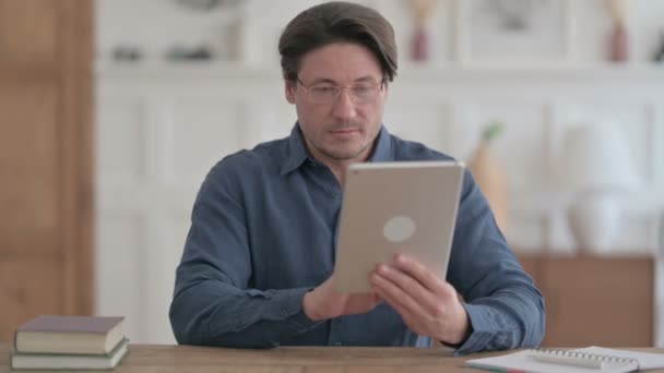 Joven usando Tablet mientras está sentado en la oficina — Vídeos de Stock