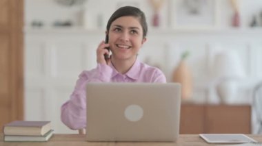 Ofiste dizüstü bilgisayar kullanırken telefonda konuşan Hintli kadın