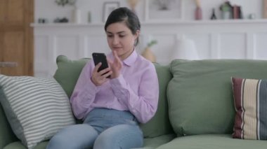 Kanepede otururken akıllı telefon kullanan Hintli kadın. 