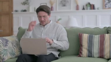 Dizüstü bilgisayarlı genç adam koltukta baş ağrısı çekiyor. 