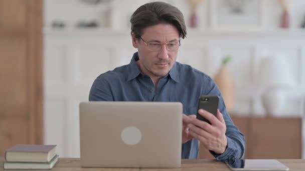 Fiatal férfi használja Smartphone használata közben Laptop az irodában — Stock videók