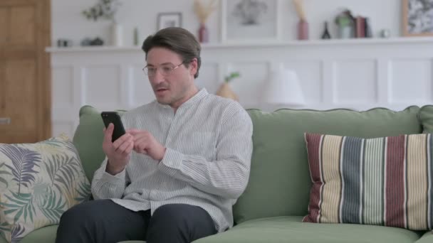 自宅でスマートフォンで成功を収めている若い男 — ストック動画