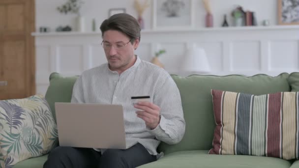 Homem jovem que faz o pagamento em linha no portátil no sofá — Vídeo de Stock