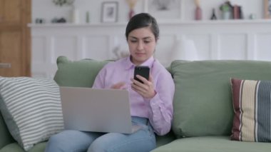 Kanepede akıllı telefon kullanan dizüstü bilgisayarı olan Hintli kadın. 