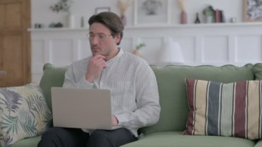Genç Düşünen Adam Kanepede Laptop 'ta çalışıyor. 