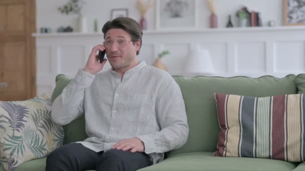 Молодой человек разговаривает по телефону на диване — стоковое видео