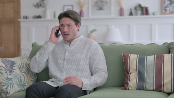Злой молодой человек разговаривает по телефону на диване — стоковое видео