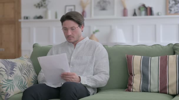 Молодой человек читает документы на диване — стоковое видео