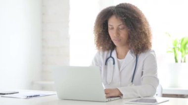 Klinikte dizüstü bilgisayar kullanırken Afrcian Doktor Başparmaklarını Aşağı Gösteriyor 