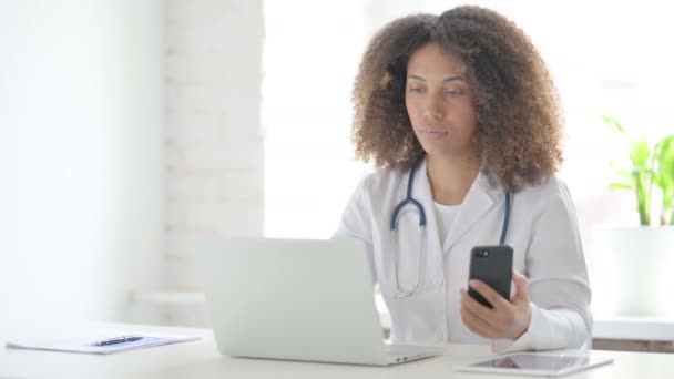 Afrcian Lekarz za pomocą smartfona podczas korzystania z laptopa w klinice — Wideo stockowe