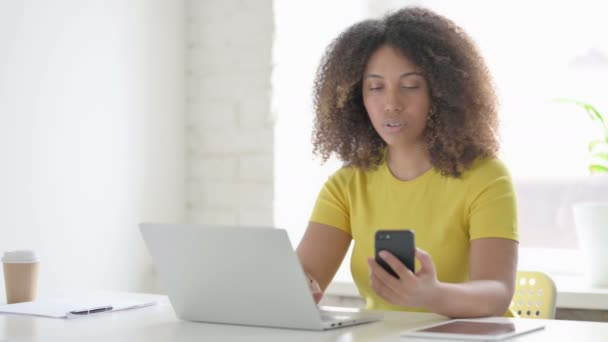 Africká žena používající smartphone při používání notebooku v kanceláři — Stock video