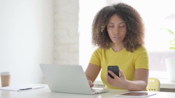 Африканская женщина разговаривает по телефону во время использования ноутбука в офисе — стоковое видео