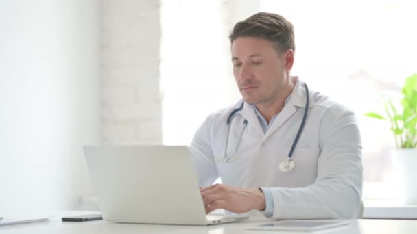 Mężczyzna lekarz patrząc w aparat podczas korzystania z laptopa w biuro — Wideo stockowe