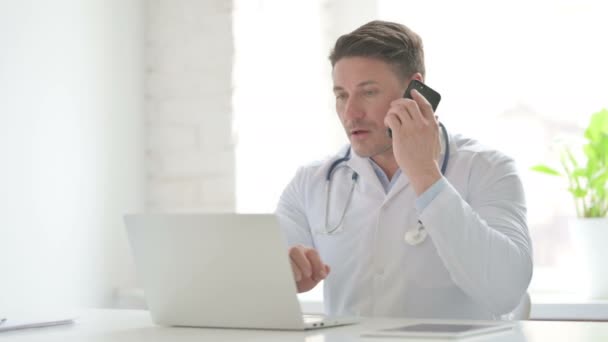 Doctor masculino con ordenador portátil hablando por teléfono — Vídeo de stock