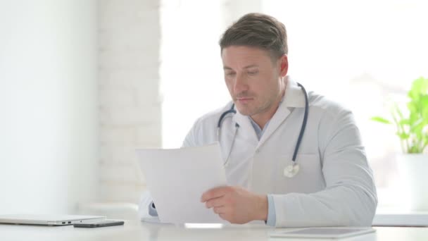 Doctor masculino leyendo documentos mientras está sentado en la oficina — Vídeo de stock