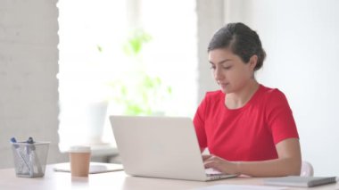 Ofiste dizüstü bilgisayar kullanırken kamerayı gösteren genç Hintli kadın.