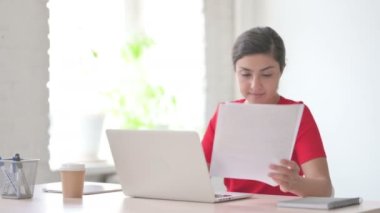 Ofiste dizüstü bilgisayar kullanırken genç Hintli Kadın Belgeleri Okuyor 