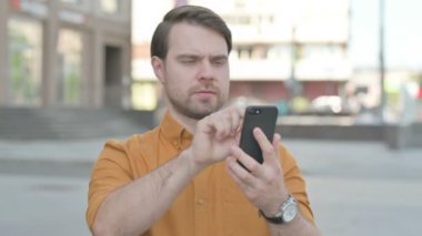 Casual Young Man Browsing Internet on Smartphone Outdoor