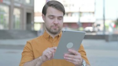 Casual Young Man Celebrating Online Win on Tablet Outdoor