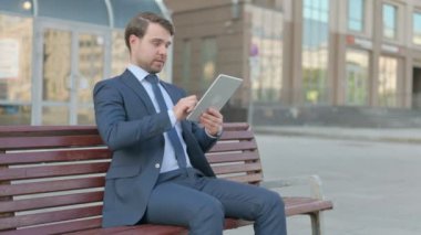 Young Businessman using Tablet while Sitting Outdoor on Bench