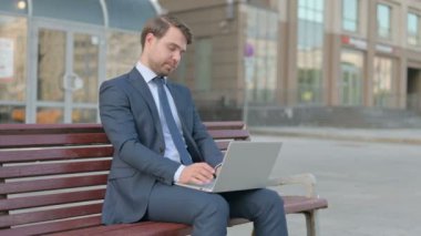 Young Businessman with Laptop Looking at Camera while Sitting Outdoor on Bench