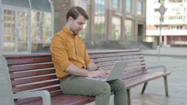 Casual Young Man with Laptop Showing Thumbs Up Sign While Sitting Outdoor on Bench 