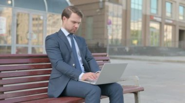 Busy Middle Aged Businessman Using Laptop Sitting Outdoor on Bench