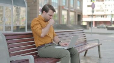 Coughing Casual Young Man Using Laptop while Sitting Outdoor on Bench