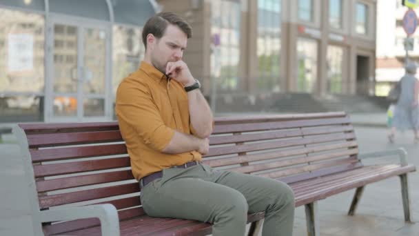 Pensive Casual Young Man Thinking While Sitting Outdoor Bench — Stockvideo