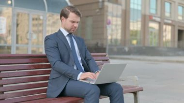 Middle Aged Businessman with Neck Pain Using Laptop while Sitting Outdoor on Bench