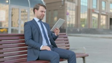 Online Video Chat on Tablet by Young Businessman Sitting Outdoor on Bench 
