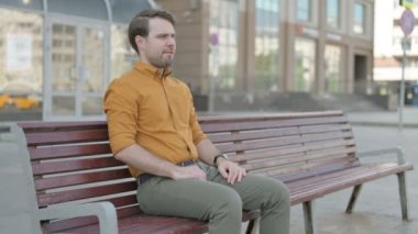 Casual Young Man having Back Pain while Sitting on Bench Outdoor