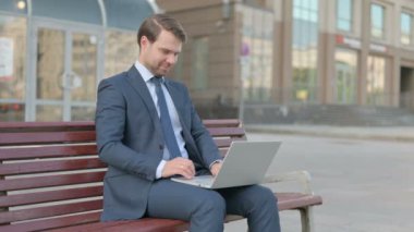 Middle Aged Businessman Talking on Video Call while Sitting Outdoor on Bench