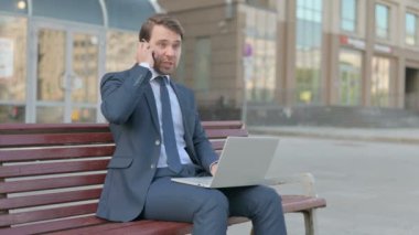 Angry Young Businessman Talking on Phone and using Laptop, Sitting Outdoor on Bench