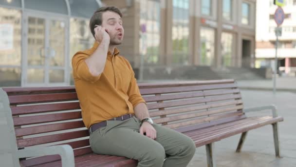Angry Casual Young Man Talking Phone While Sitting Outdoor Bench — 图库视频影像
